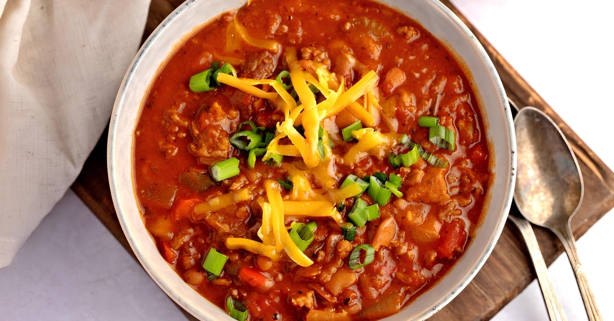 A bowl of delicious spicy homemade boilmaker chili with ground meat, sausage, green onions, tomatoes and cheese