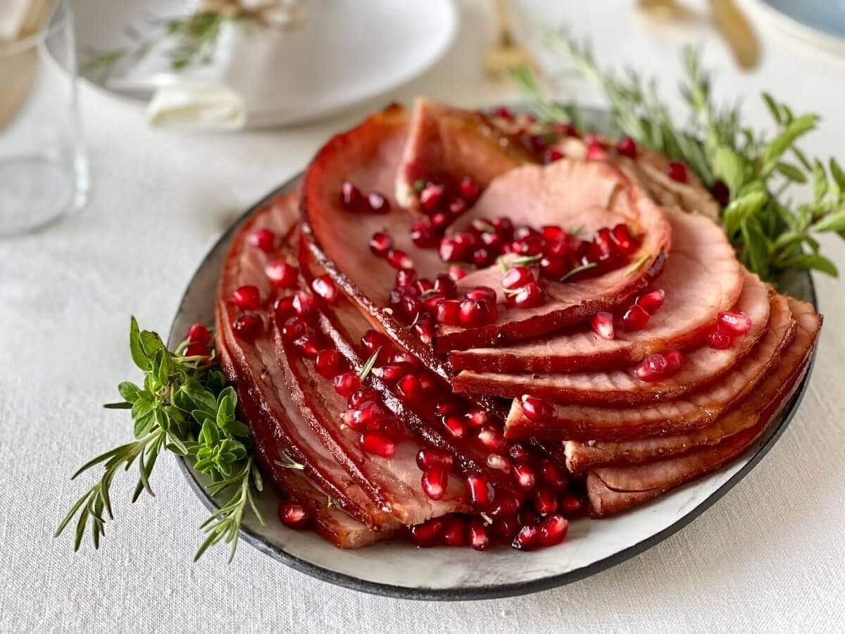 Sliced ham garnished with pomegranate arils on a holiday plate. 