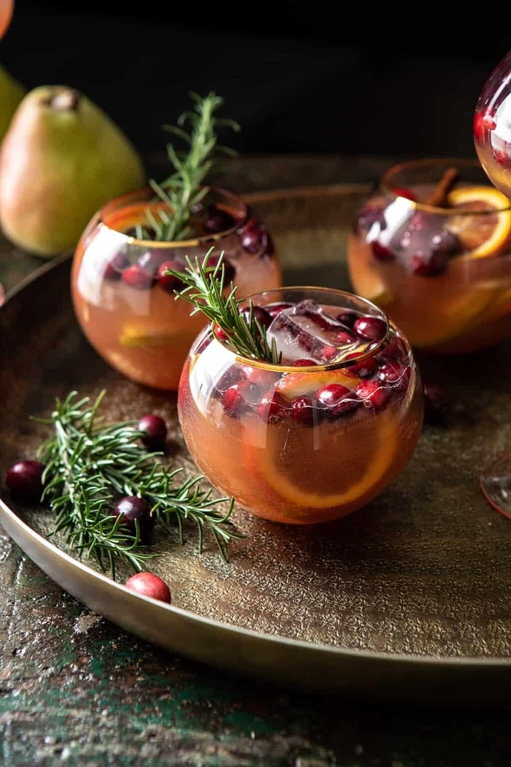 Glasses of sangria with cranberries, slices of pear, orange and ice.