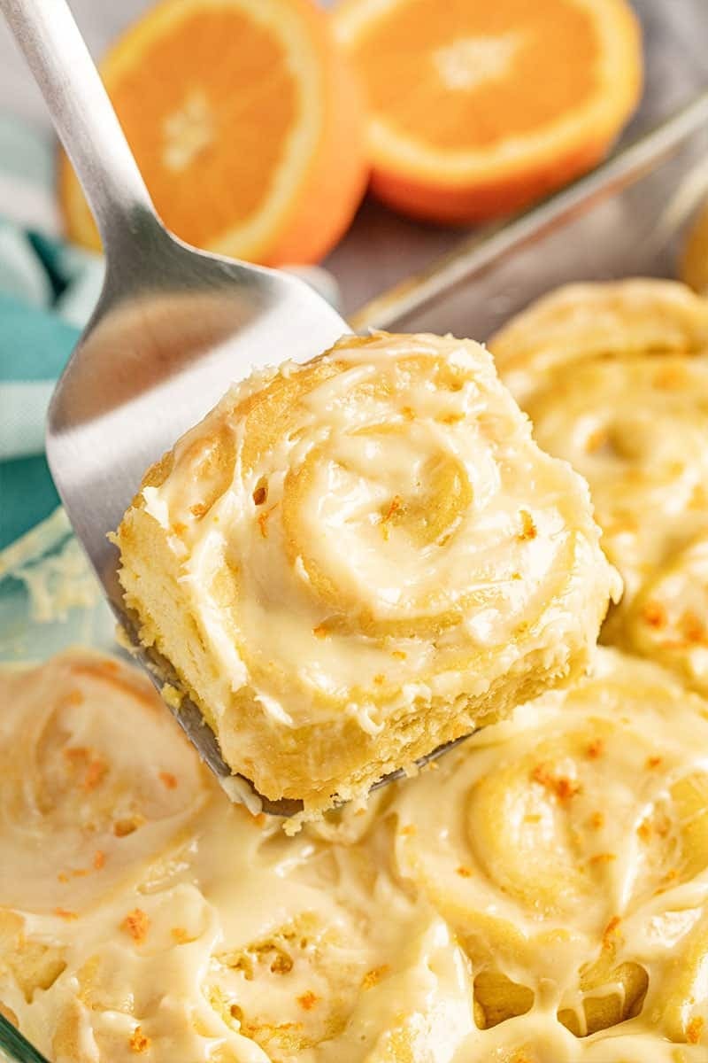 Ladle scooping orange rolls with orange cream glaze on top. 