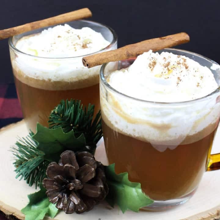 Two glasses of rum punch with cinnamon stick, whipped cream and pinecones beside.