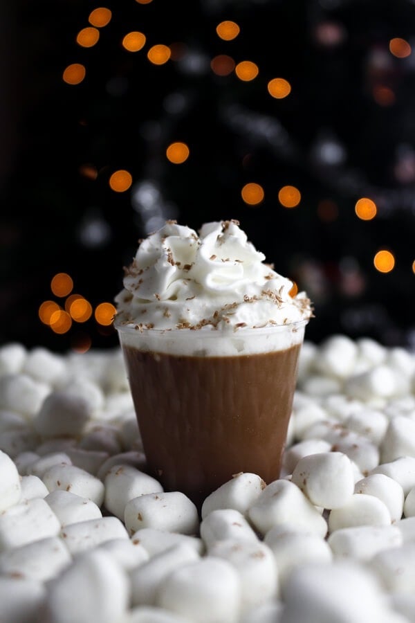 Chocolate Jello shots on plastic cup topped with whipped cream surrounded with a bunch of marshmallows.