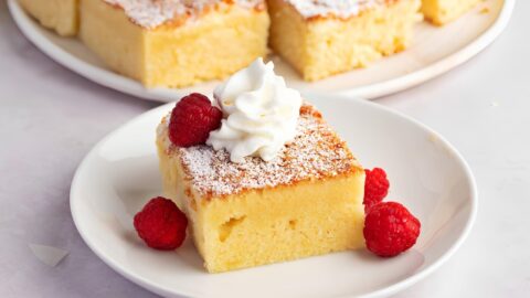 Slice of hot milk cake garnished with whipped cream, powdered sugar and berries.