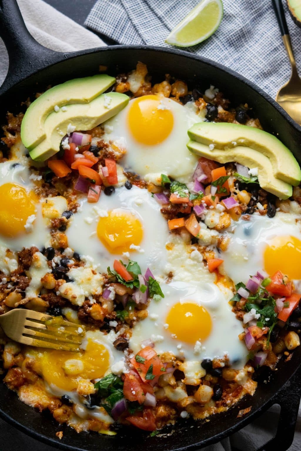 Breakfast casserole cooked in skillet loaded with sliced avocado, chorizo, hominy, black beans, and eggs.