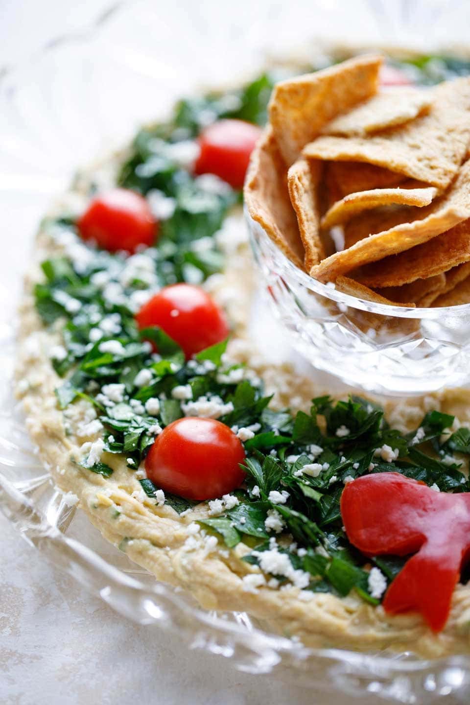 Hummus topped with chopped parsley and sliced tomato cherries served with chips. 