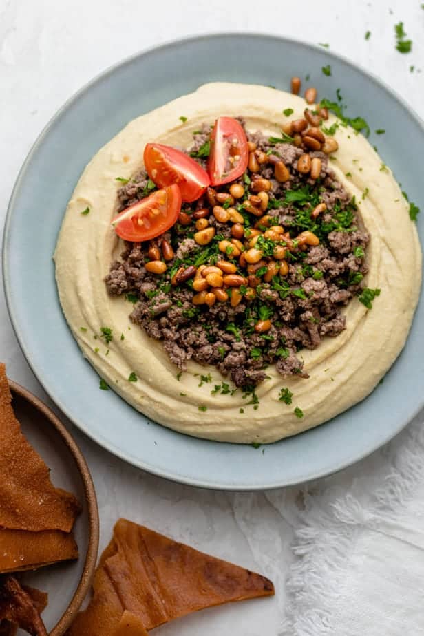 Hummus Bowl Topped with Seasoned Ground Beef, Toasted Pine Nuts, Herbs, and Tomato Wedges
