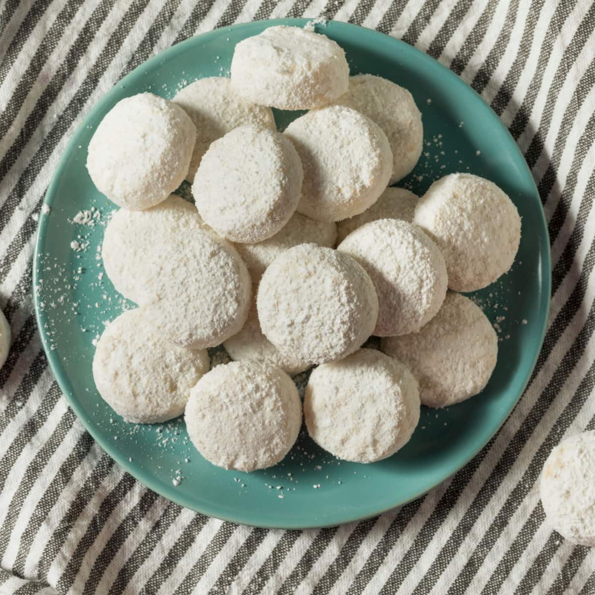 A bunch of powdered sugar coated Italian wedding cookies in plate. 