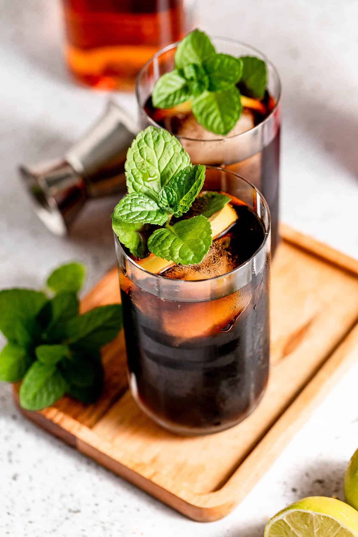Boozy and refreshing jack and coke cocktail with mint and lemon on a wooden serving tray