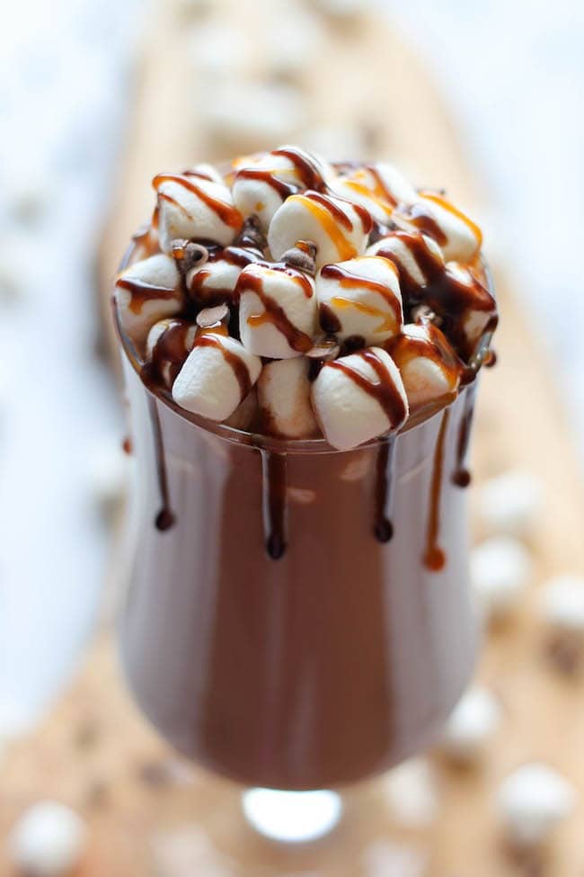 Chocolate drink on a tall glass topped with Topped with marshmallows and drizzled with caramel syrup.