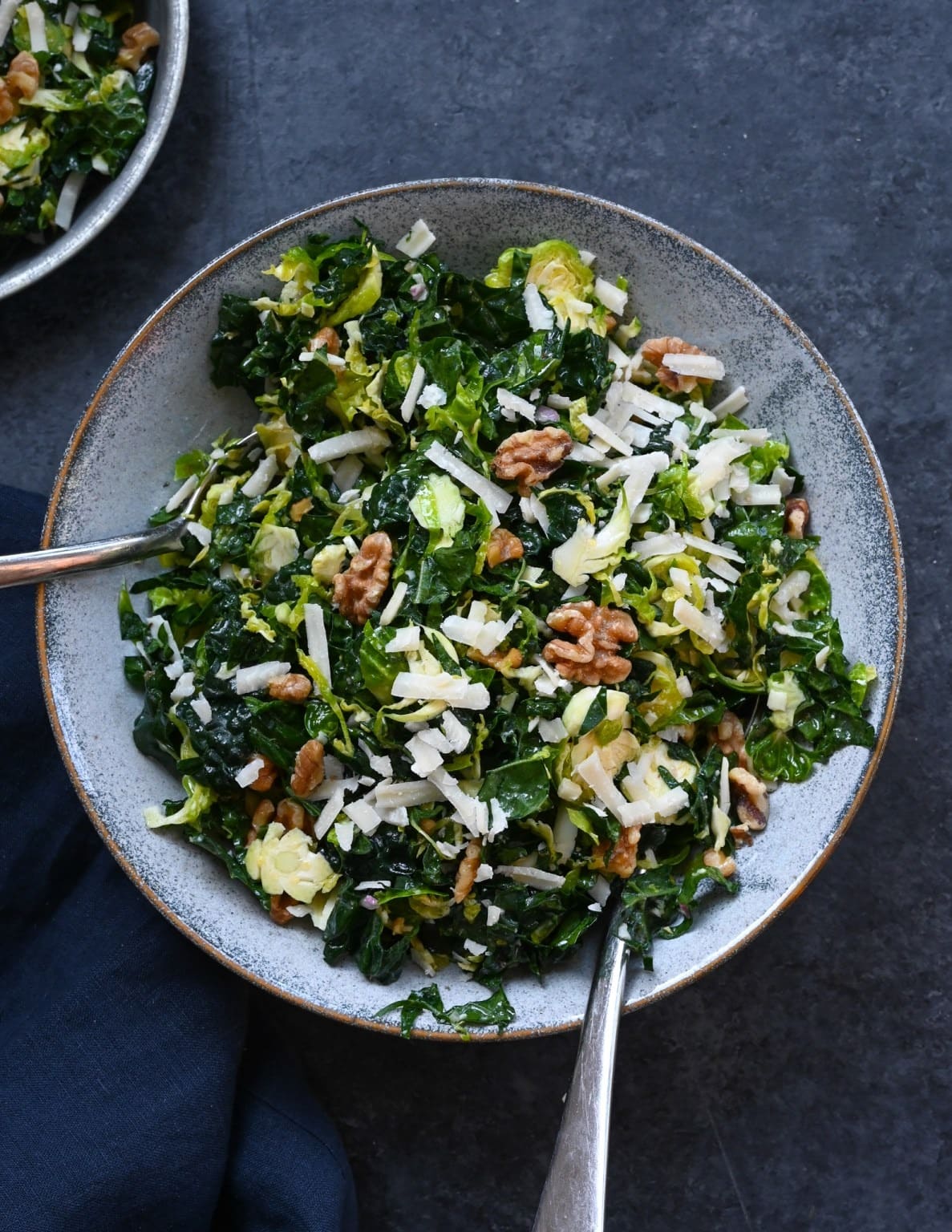 Kale & Brussels Sprout Salad with toasted walnuts, chunks of Parmesan and a lemony Dijon dressing served on a plate 