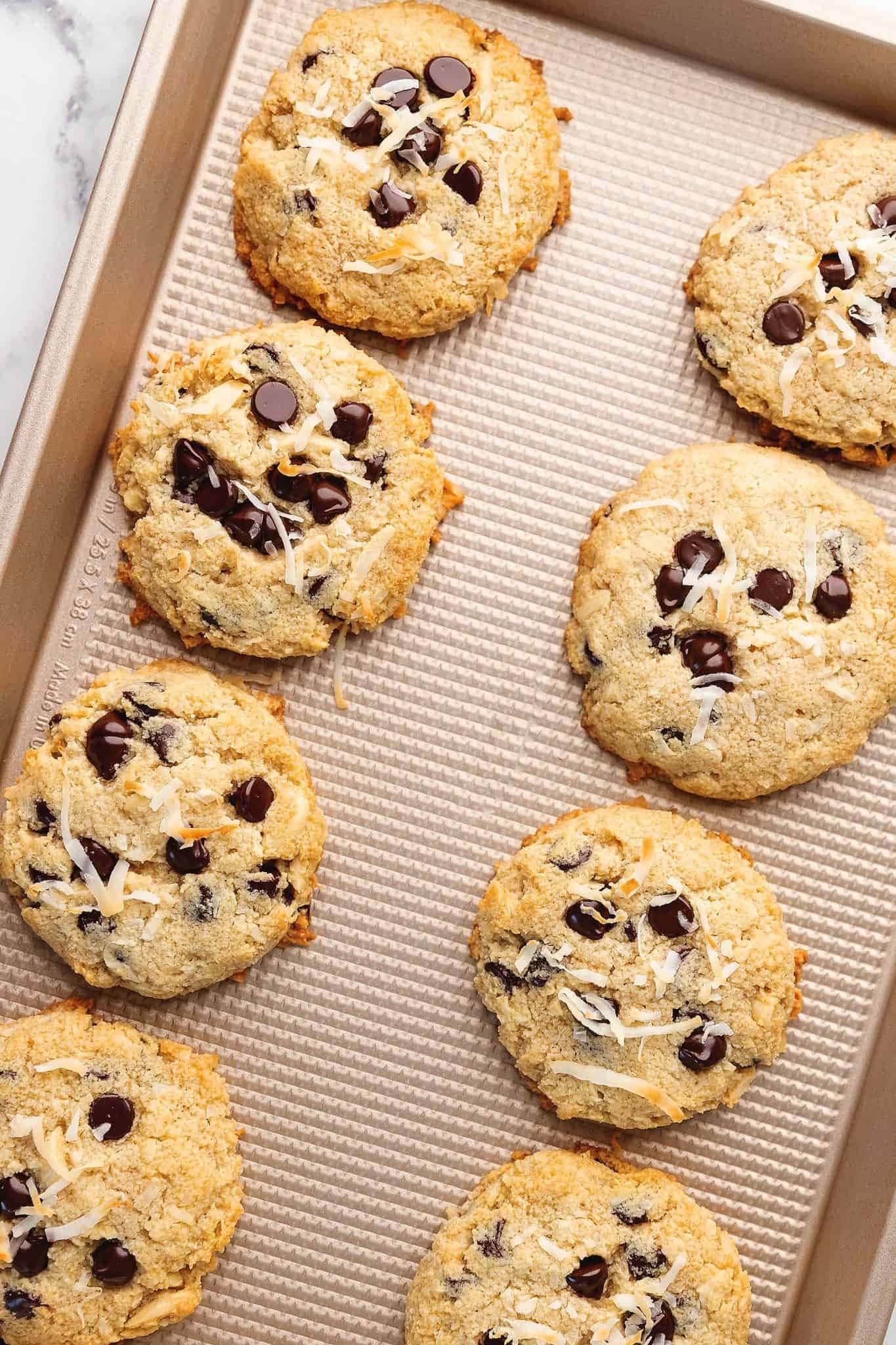 Chocolate chip cookies topped with shredded almonds on a sheet pan.