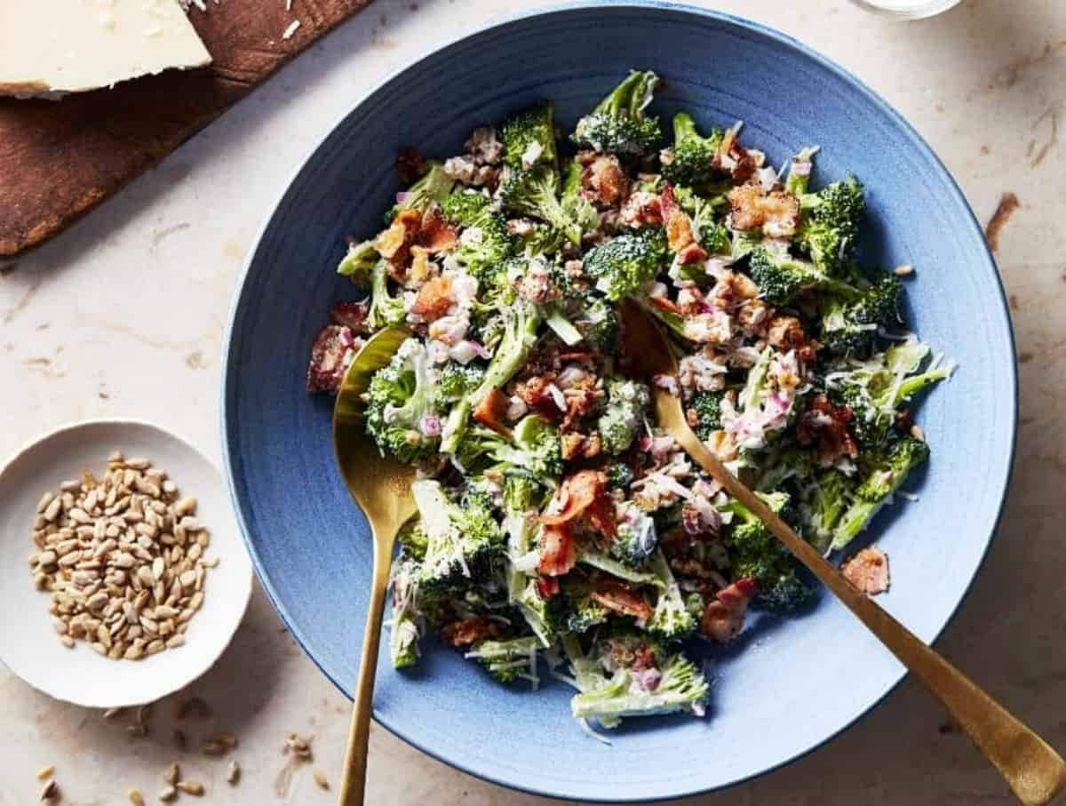 Top view of broccoli salad with bacon served on a blue plate with spoon and fork. 