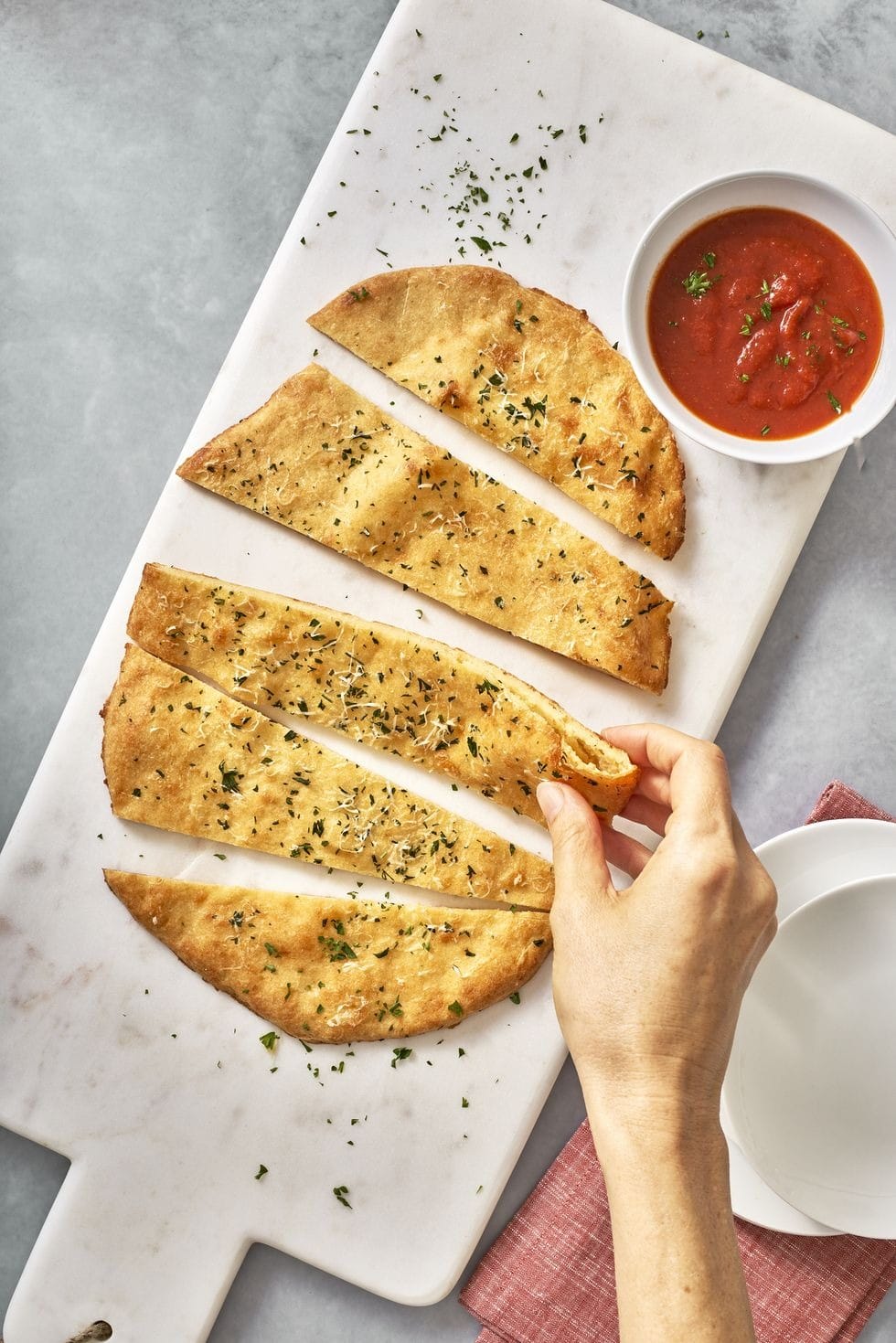 Sliced garlic bread on a cutting board with dipping sauce. 