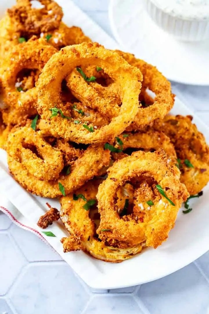 Bunch of breaded onion rings served on a plate.