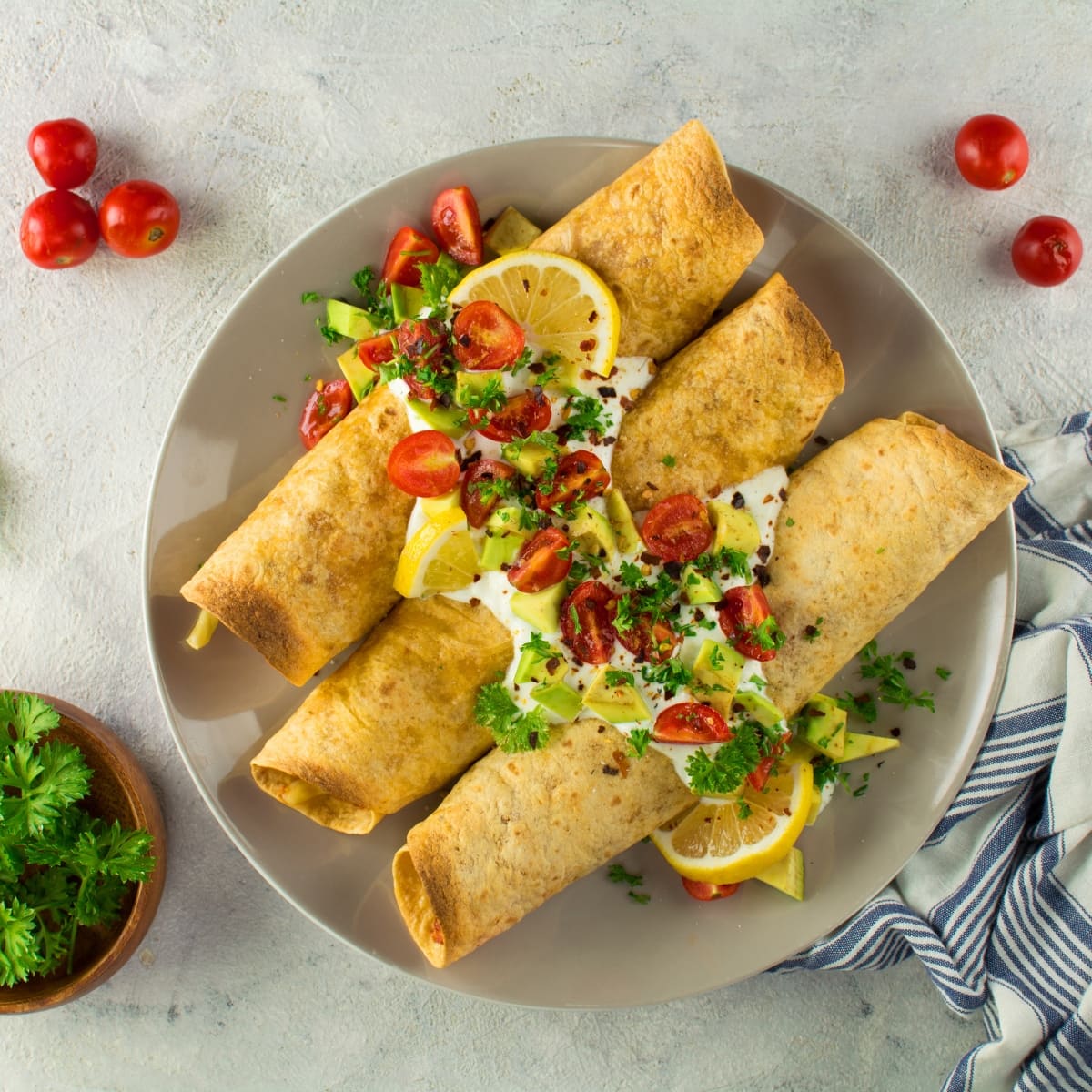 Taquitos with Tomatoes, Avocado, Crema, Lemon, and Onions on a Plate