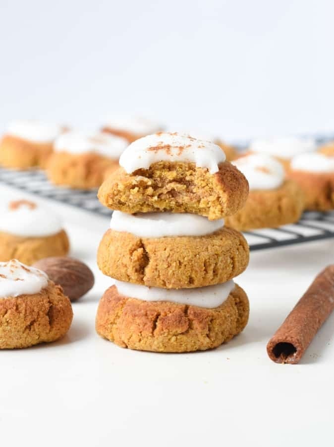 Pumpkin cookies with cream toppings stacked on a white surface. 