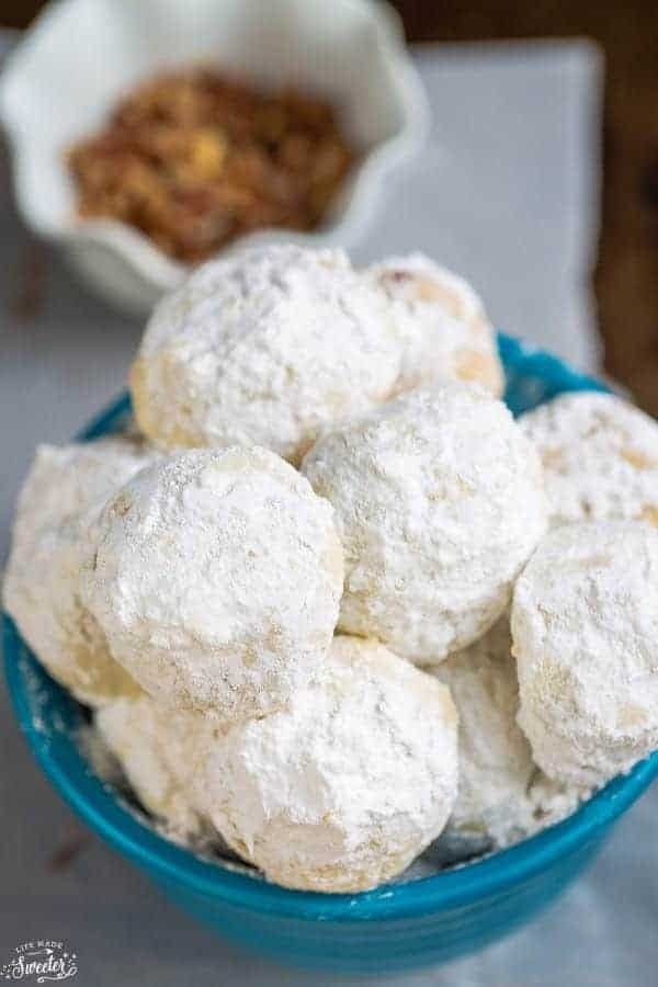 Bunch of ball-shaped cookies covered in powdered sugar served on a blue bowl.