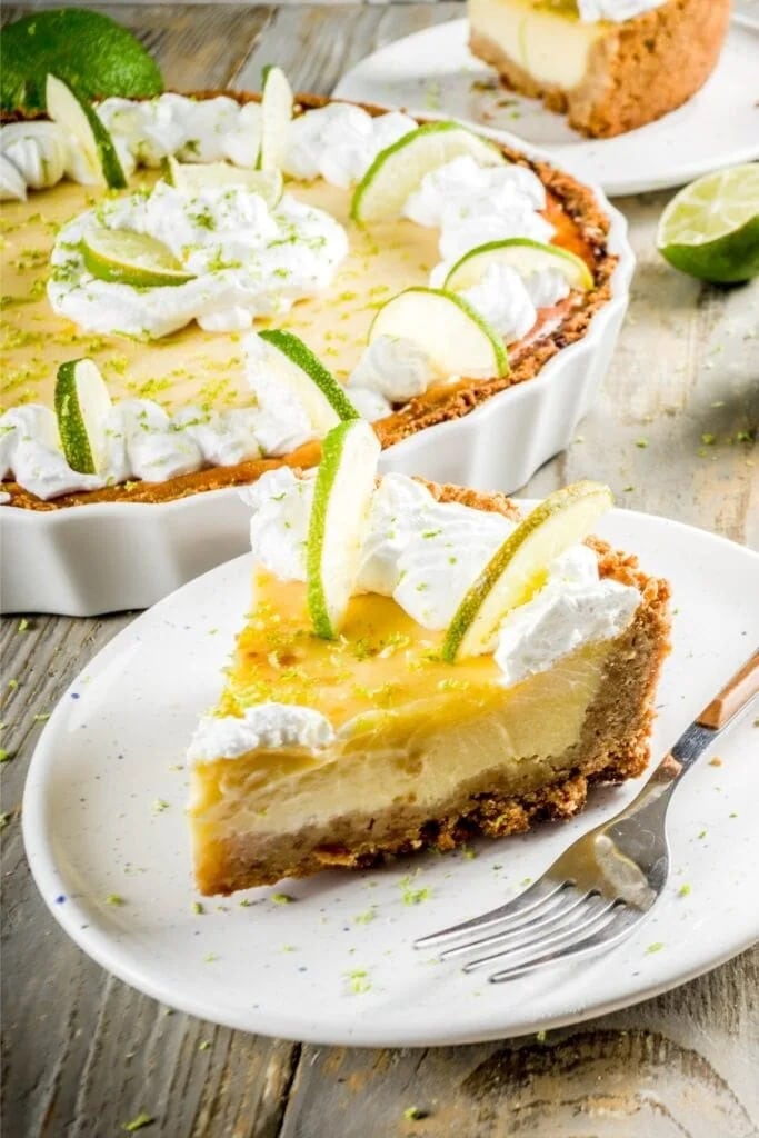 A serving slice of key lime pie with lime slices and whipped cream toppings. 