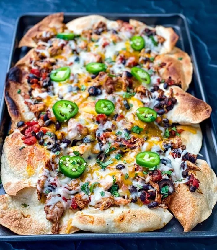 Nachos with turkey, tomatoes, onions, olives, chiles, cream and cheese filling arranged on a pan. 