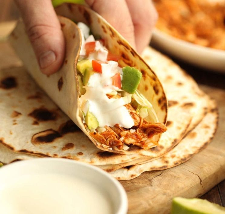 Hand picking a taco with turkey, sliced avocado, tomatoes and cream filling. 