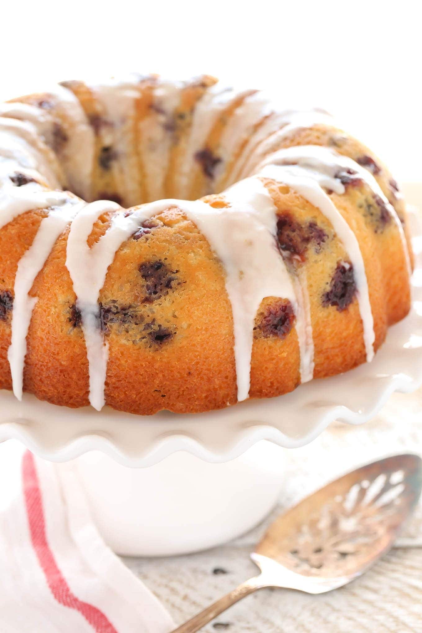 Bundt cake with blueberries and sugar glaze on top placed on a cake tray. 