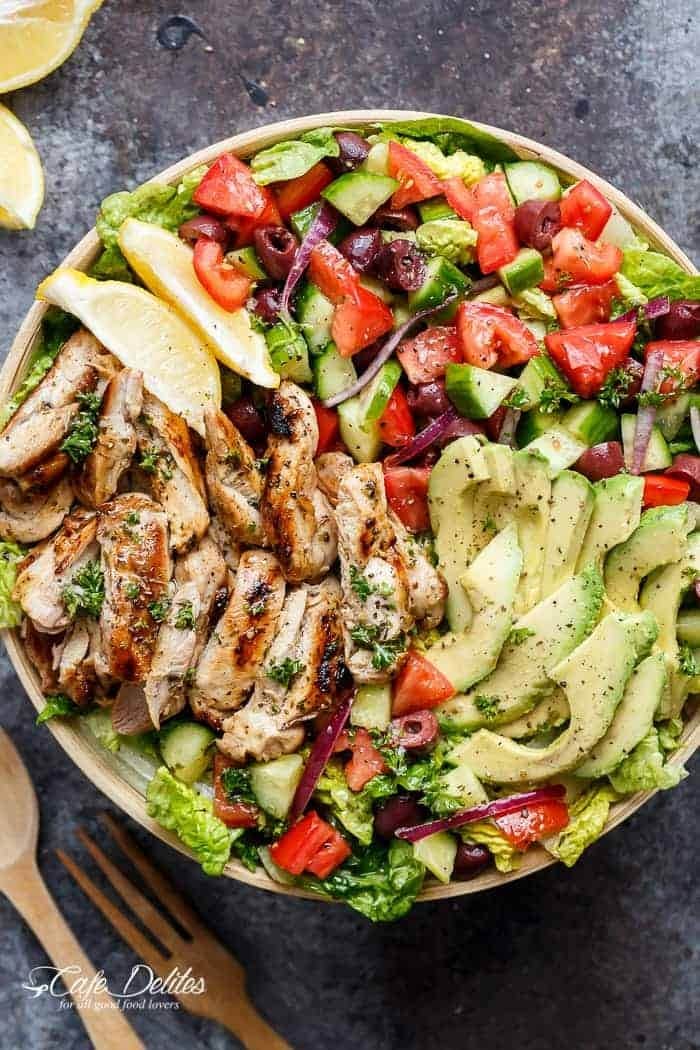 Bowl of salad with grilled chicken strips, slice lemons, avocados. diced cucumber, tomatoes and Kalamata olives