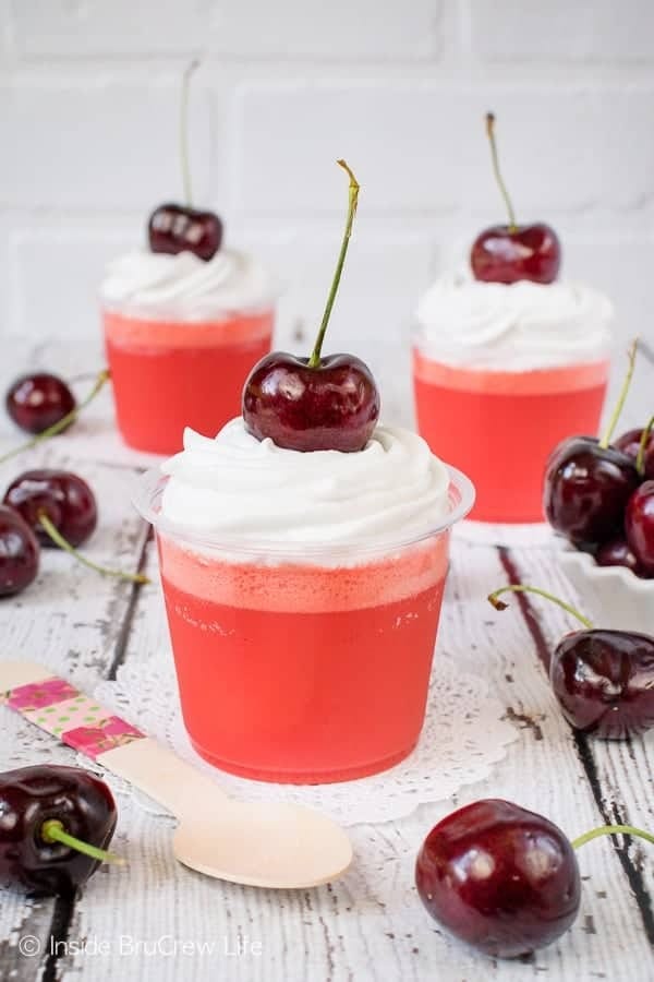 Jello parfaits in a plastic cup topped with whipped cream and fresh cherries.