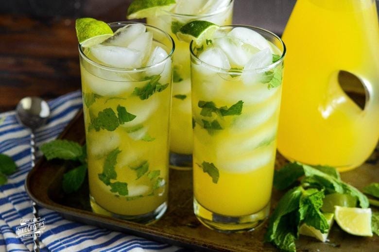 Three glasses of refreshing lemonade with slices of lime and sprigs of mint.