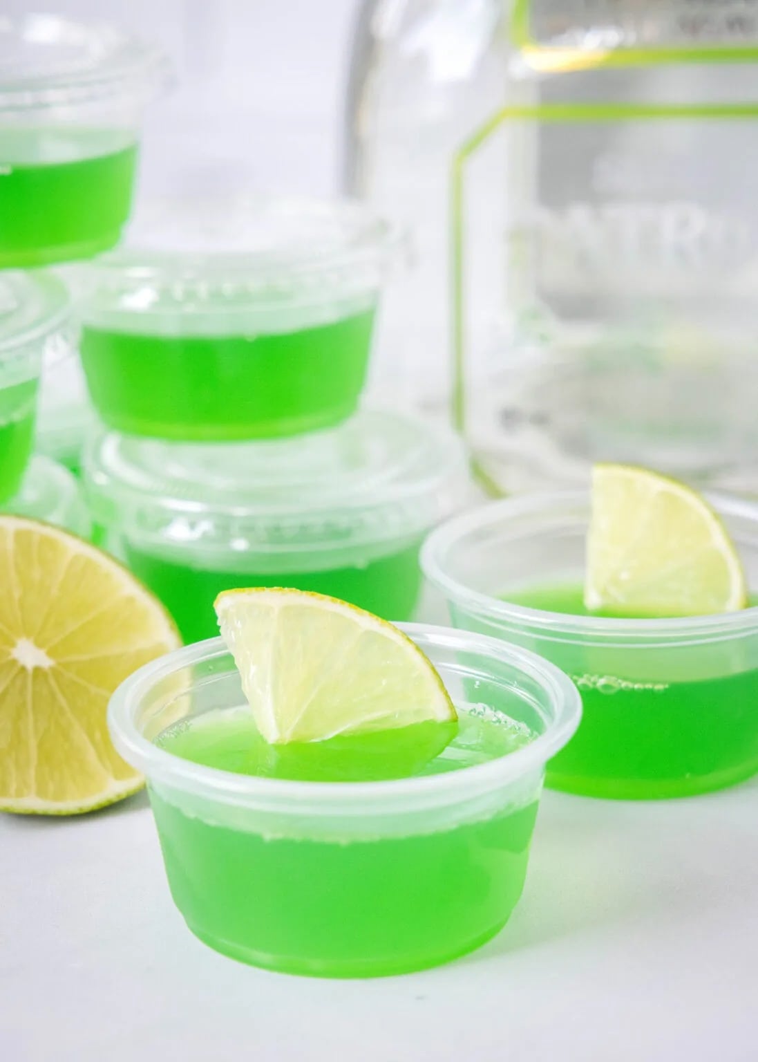 Green colored Margarita Jello shots garnished with lemon slices on a plastic cup. 