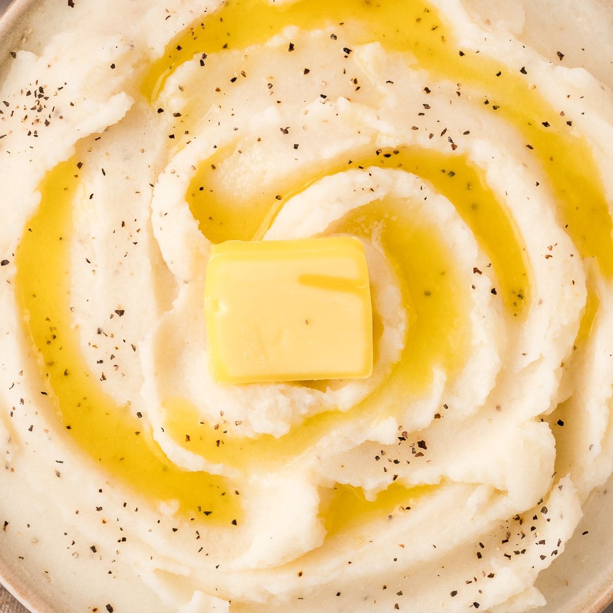 Close up of creamy mashed potato with butter and pepper.