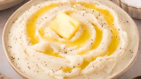 Mashed potatoes with butter and pepper served in a brown bowl.