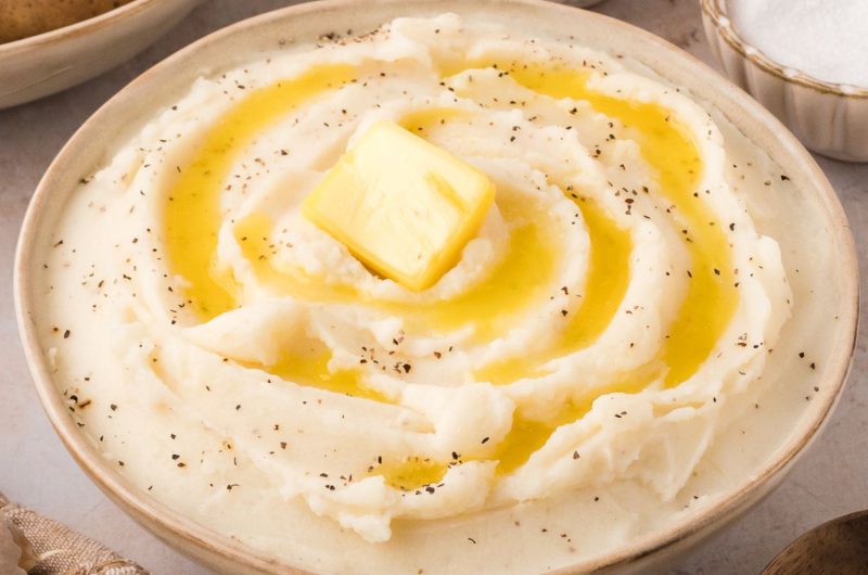 Mashed potatoes with butter and pepper served in a brown bowl.
