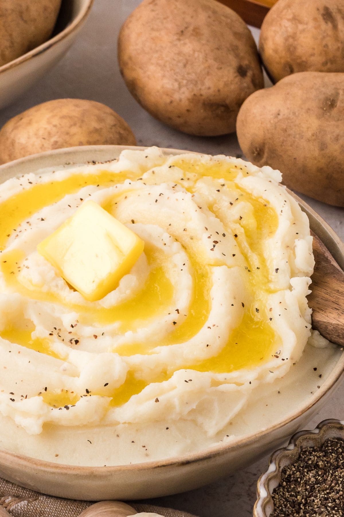 Mashed potato in a brown bowl with butter on top.
