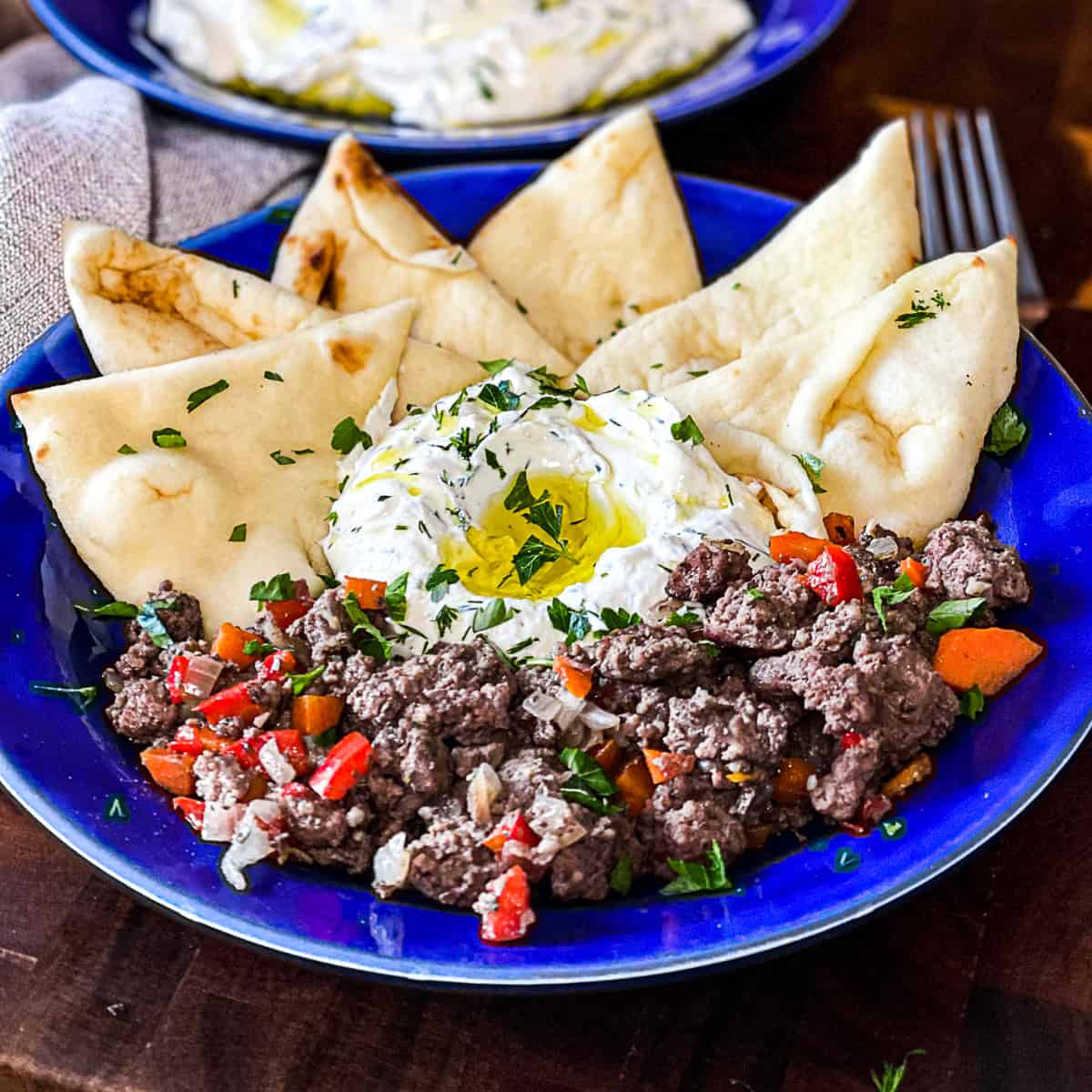 Mediterranean Ground Beef and Yogurt Platter with Seasoned Ground Beef and Peppers, Yogurt Sauce with Oil and Parsley, and Fresh Triangles of Pita on a Plate