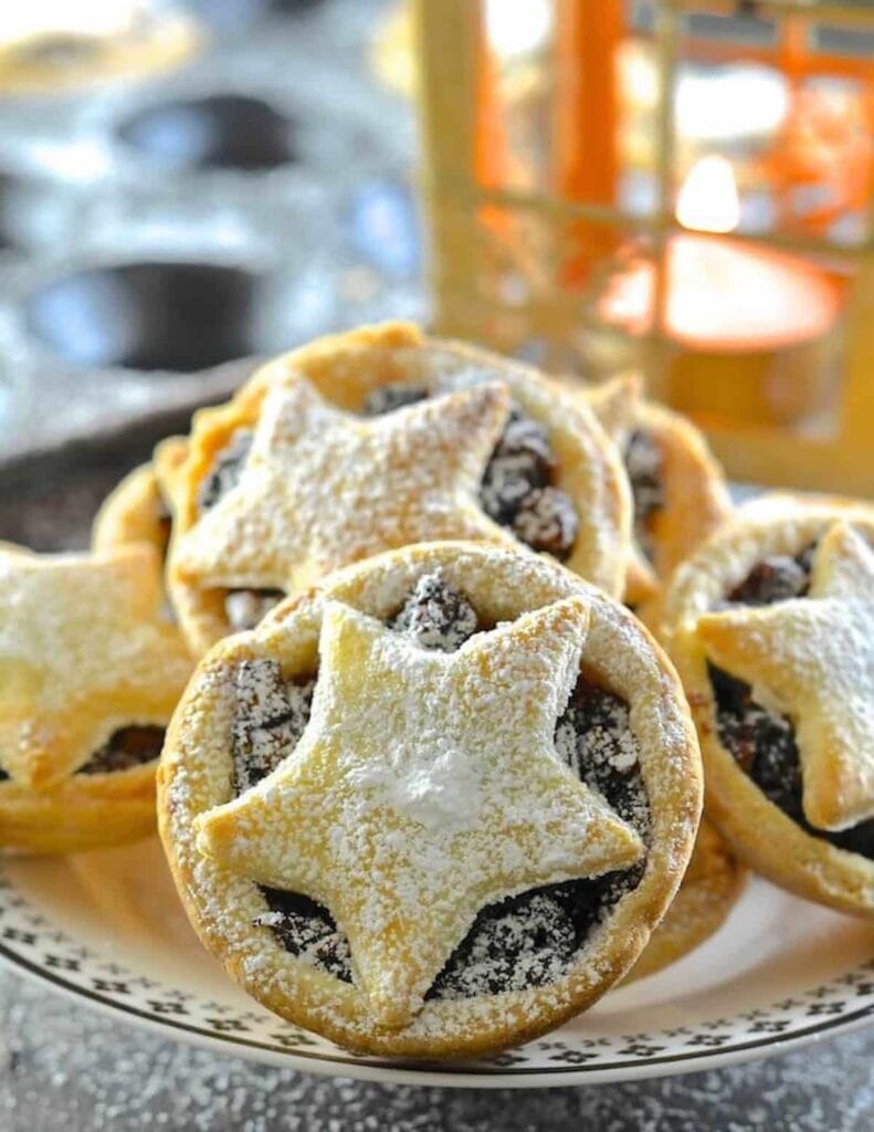 Bunch of mince pies covered with powdered sugar served on a plate.