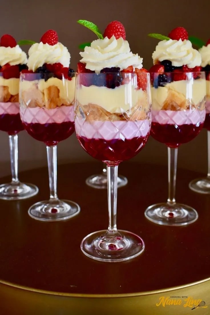 A delicious trifle dessert on wine glasses with layers of sponge cake, custard, fresh fruits, and whipped cream.