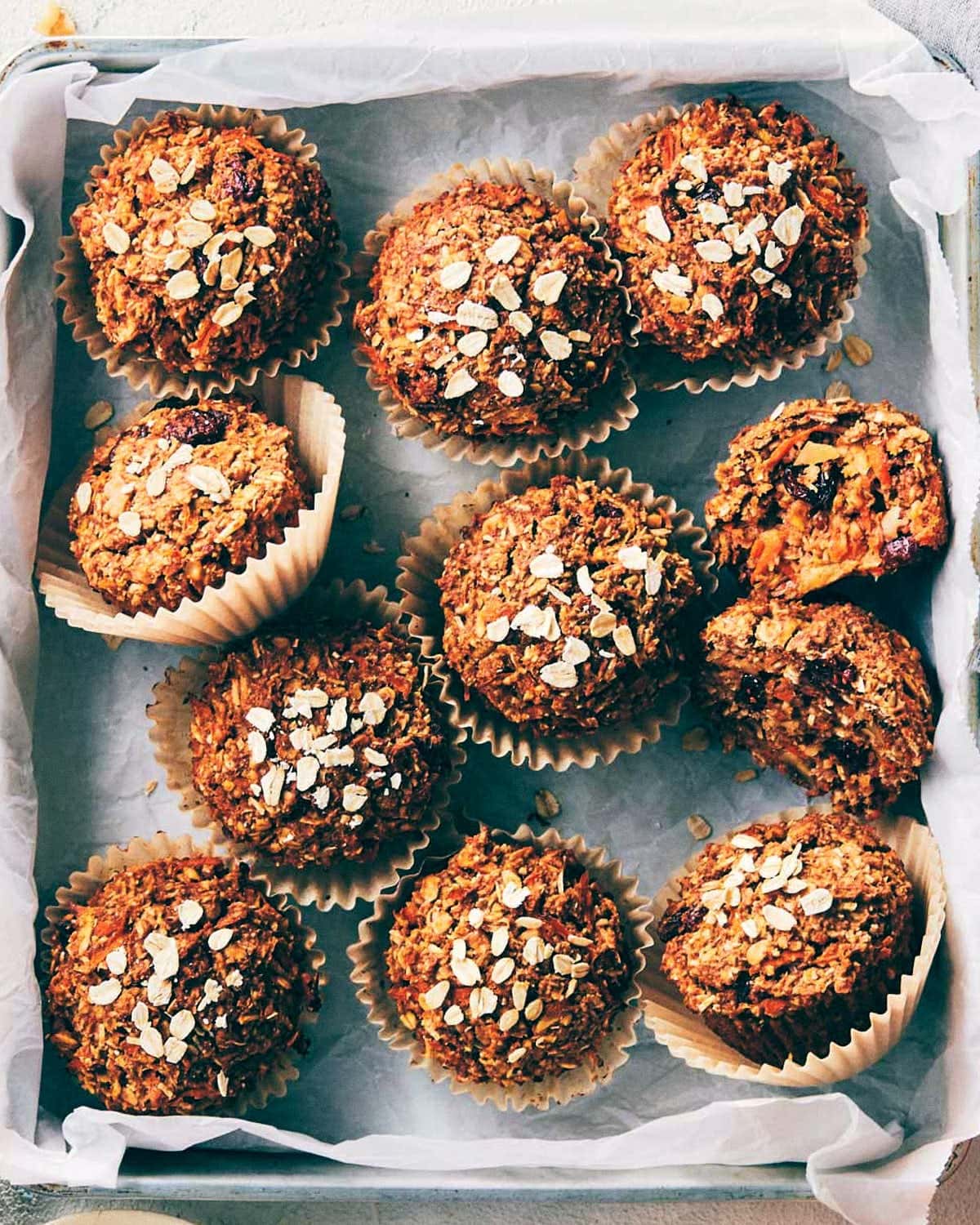 Bunch of breakfast muffins are with oats, apples, carrots and cranberries on a baking pan.