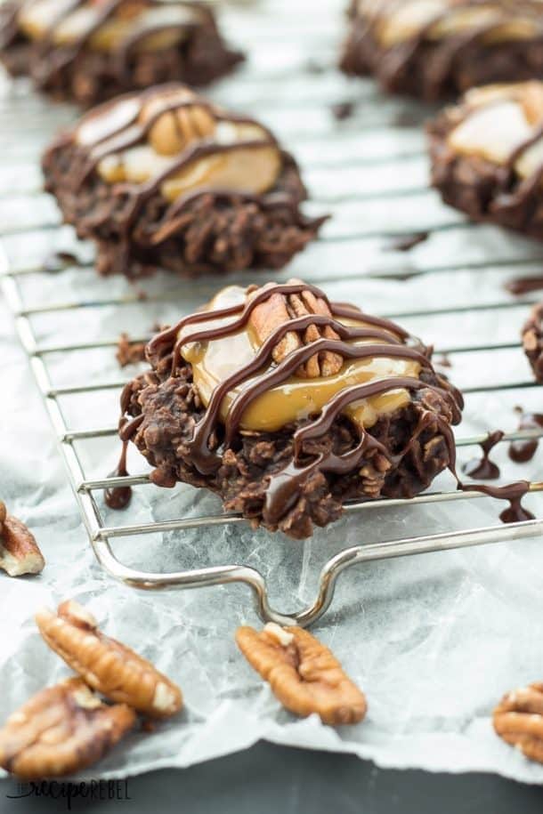 Turtle cookies with pecan nuts on top drizzled with chocolate syrup on a cooling rack. 