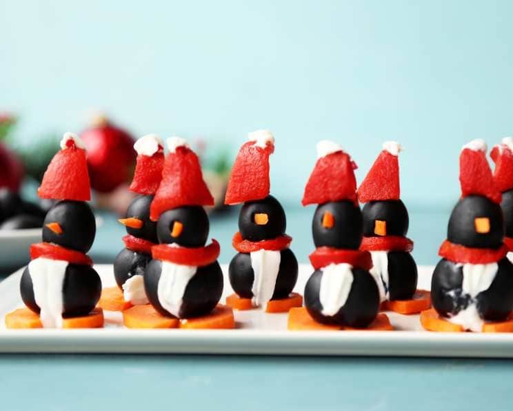 Penguin shaped appetizers arranged on a plate made with olives, carrots, pimento peppers and cream cheese.
