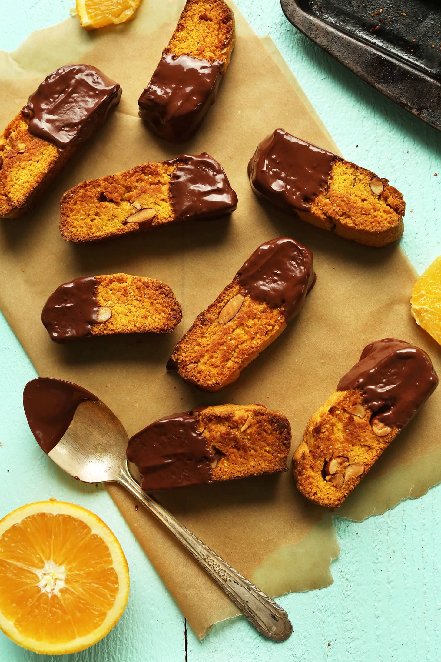 Pieces of orange biscotti half dipped on chocolate syrup laid on a brown parchment paper. 