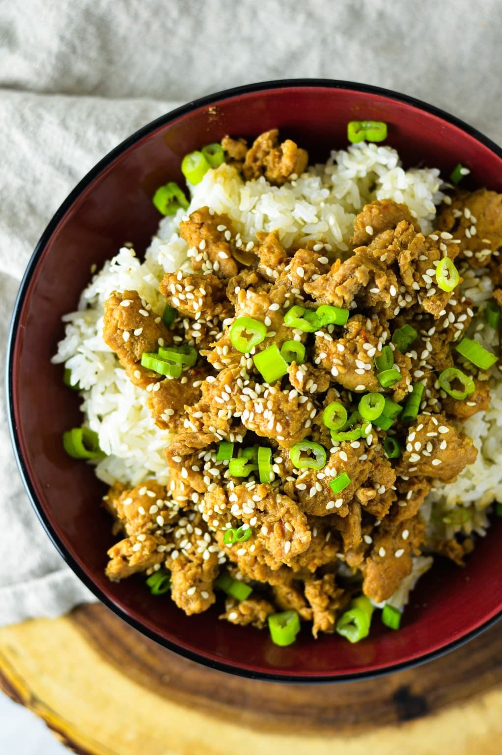 White rice in a bowl topped with ground chicken garnished with sprinkle of sesame seeds and chopped green onions.