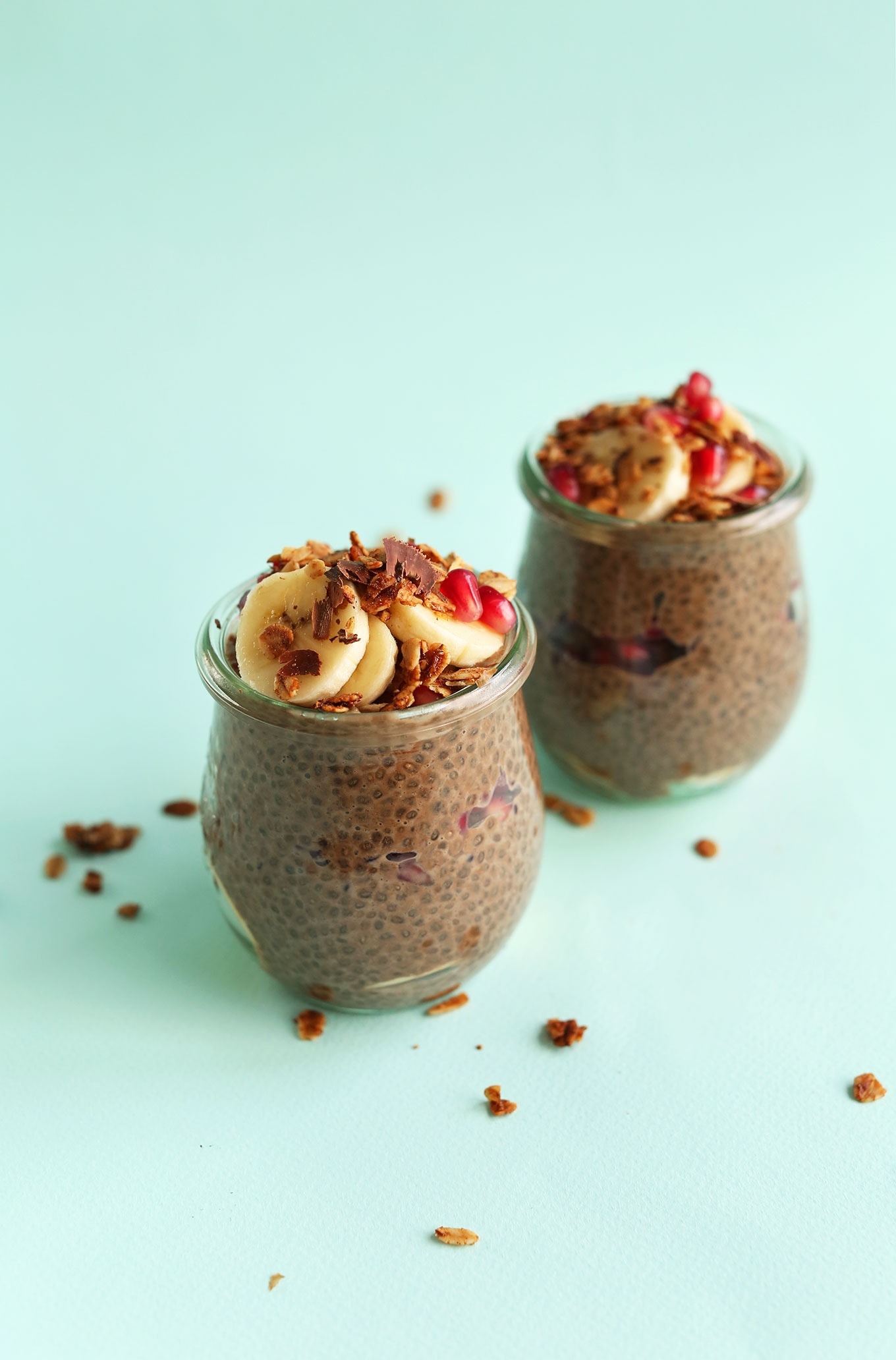 Two small jars of overnight chocolate with chia seeds pudding topped with sliced bananas and shredded chocolate.
