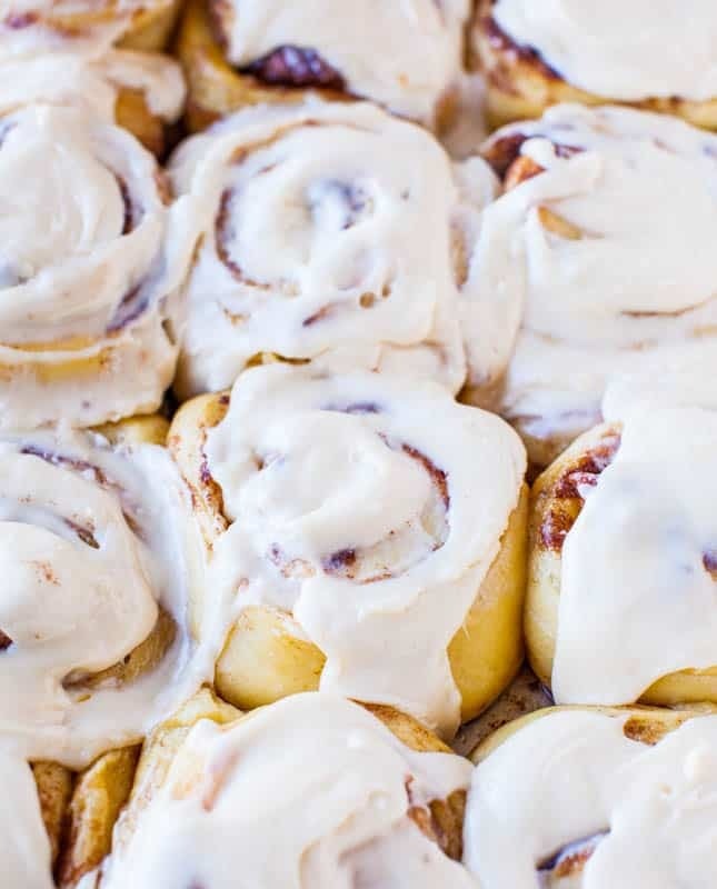 Freshly baked cinnamon rolls on a baking tray with frosting on top