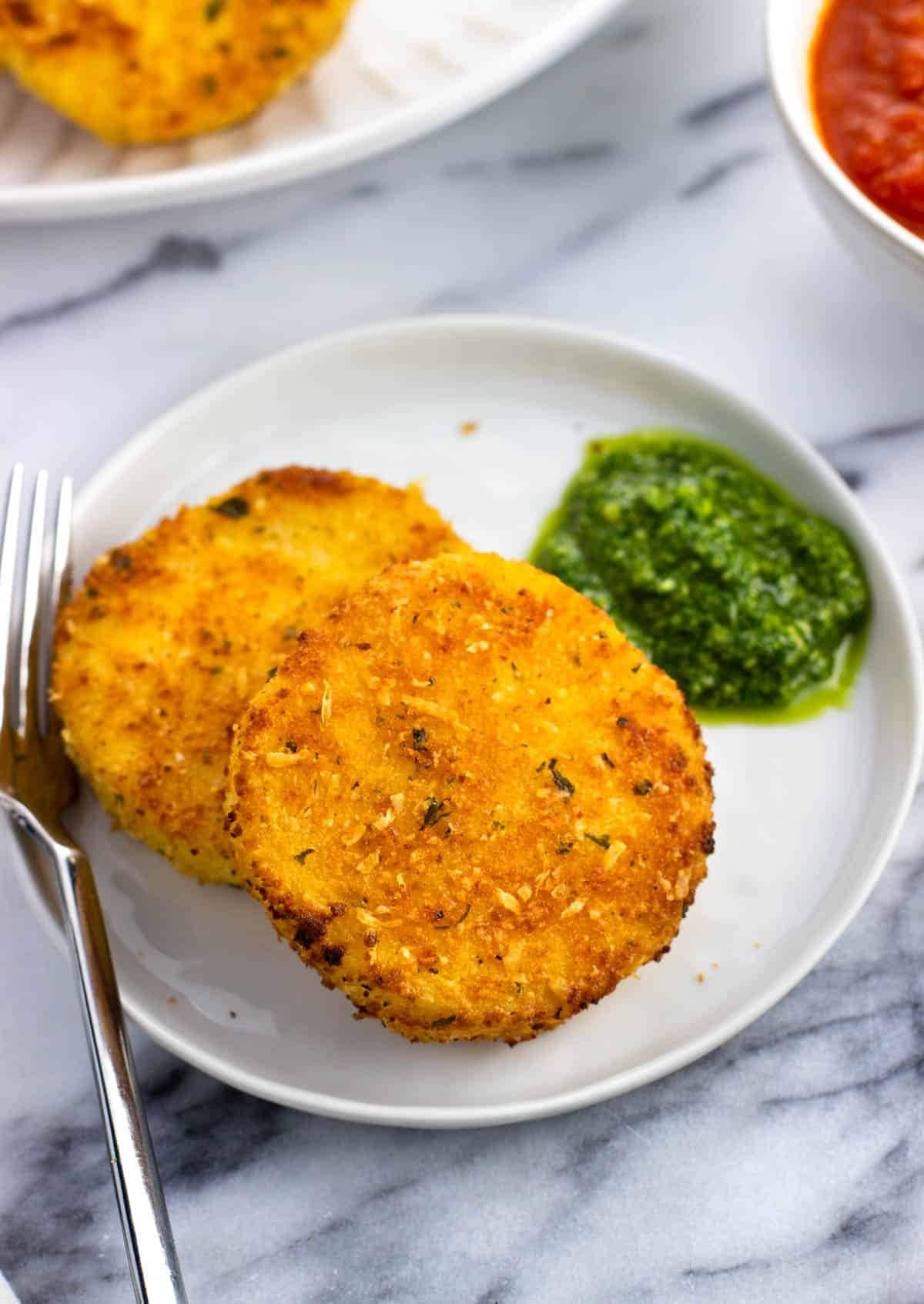 Breaded pan fired polenta slices served with pesto sauce on a white plate. 