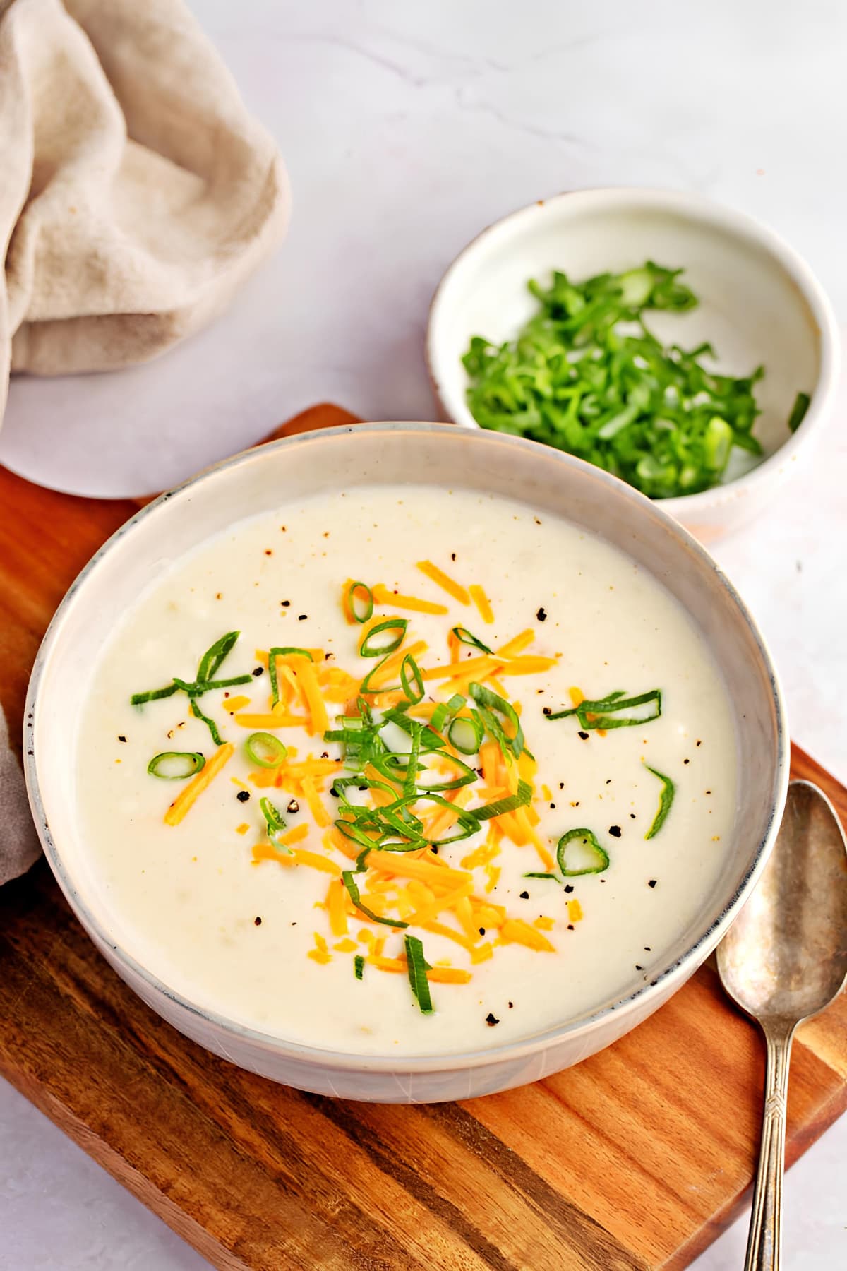 Potato soup in a bowl garnished with cheese and chopped onion leaves. 