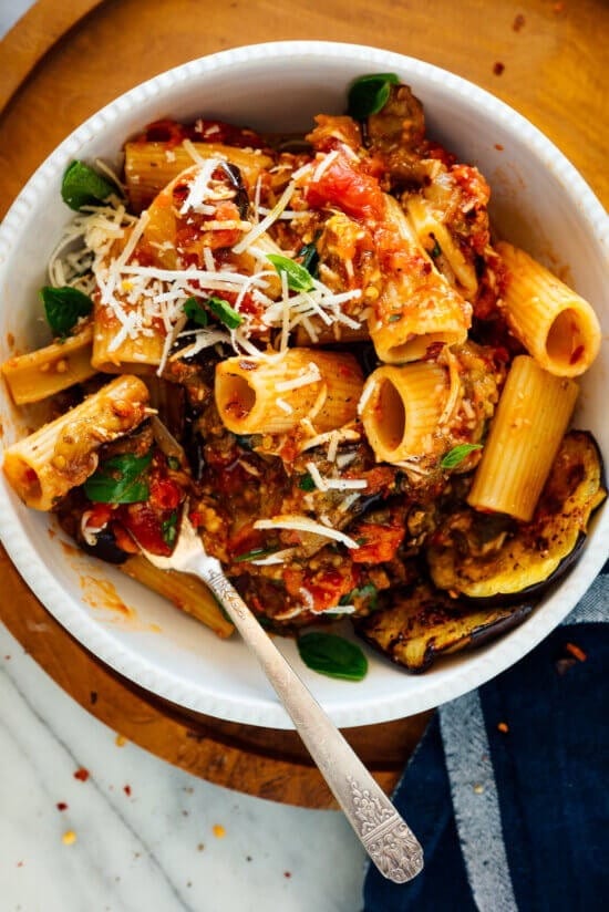 Pasta with roasted eggplant, sauce and grated cheese served on a small white bowl. 