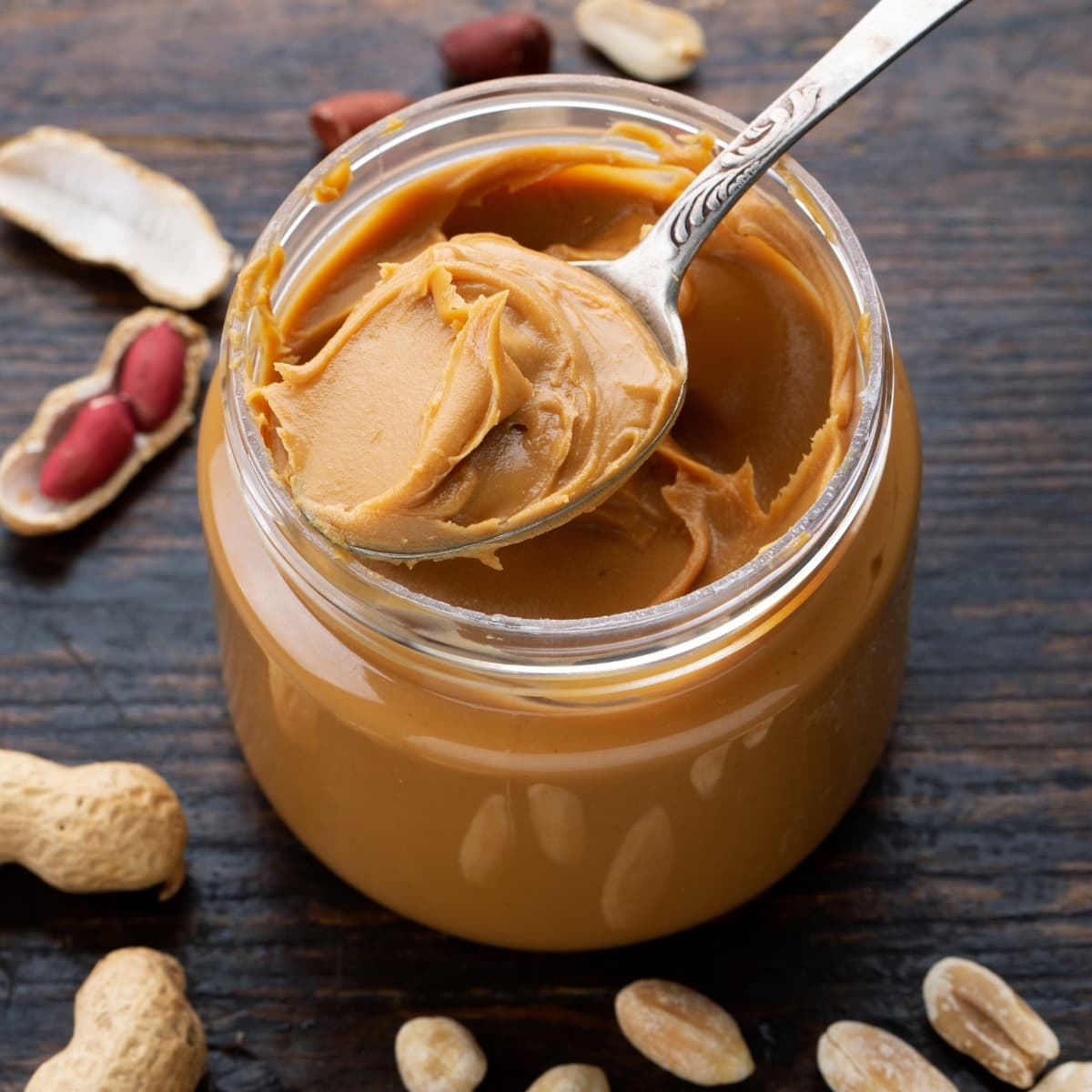 Peanut butter in a jar with a spoon on a wooden table