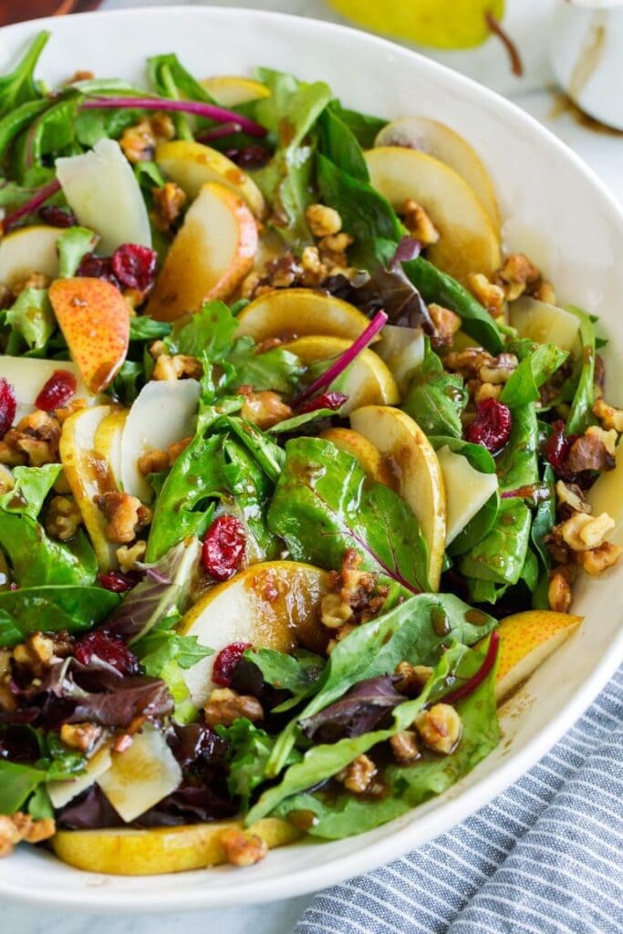 Autumn pear salad with candied walnuts and balsamic vinaigrette on a white bowl.