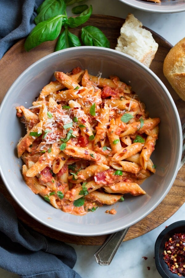 Penne pasta tossed on a tomato sauce served on a bowl garnished with cheese and herbs. 