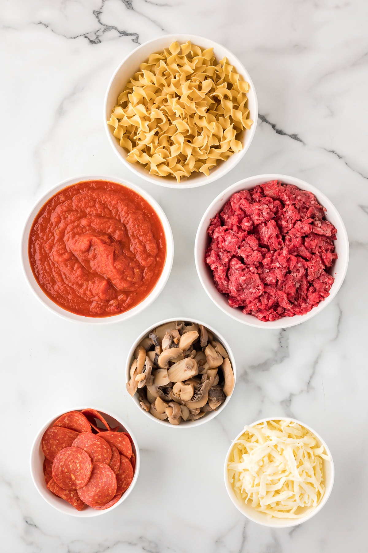 Ingredients for Pepperoni Pizza Casserole - ground beef, egg noodles, tomato sauce, mushrooms, pepperoni, mozzarella